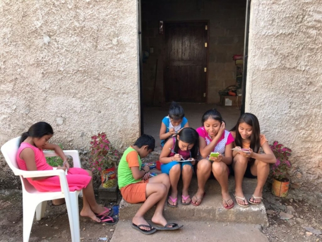Six Mayan children drawing, sitting on doorstep