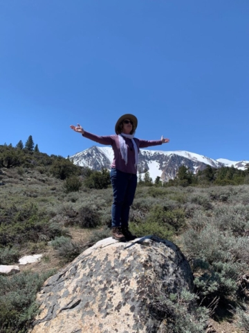 Ruth standing on rock with arms outstretched, mountain in background